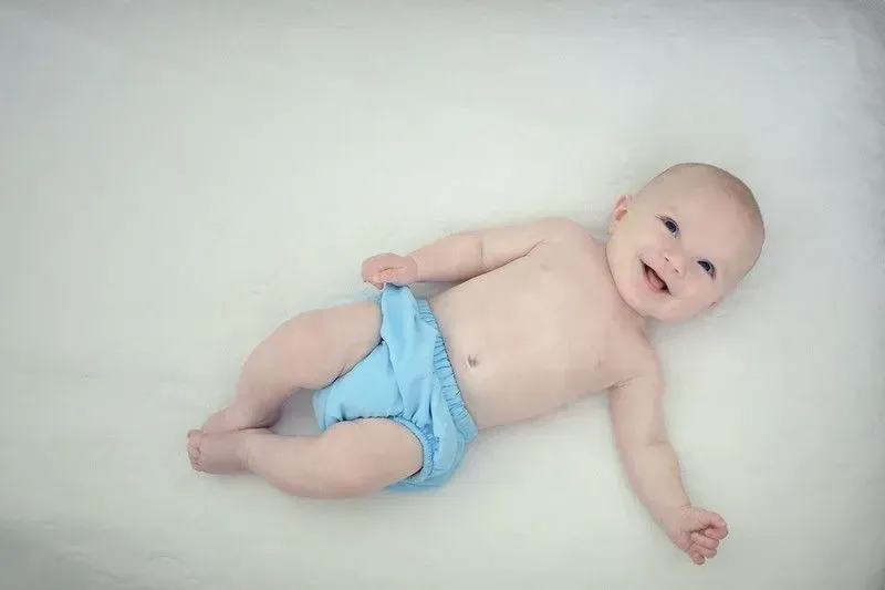 A baby wearing a blue nappy smiles up at the camera.