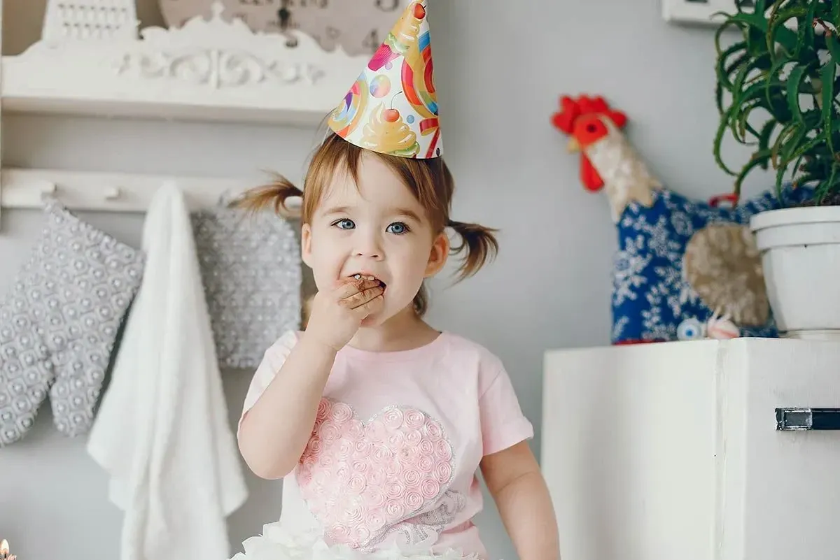 A little girl wearing a party hat eating a slice of Trolls cake.