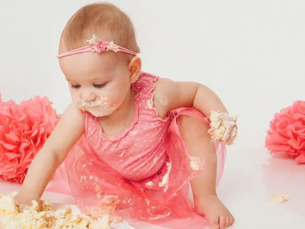 A little girl in a pink dress eating birthday cake.