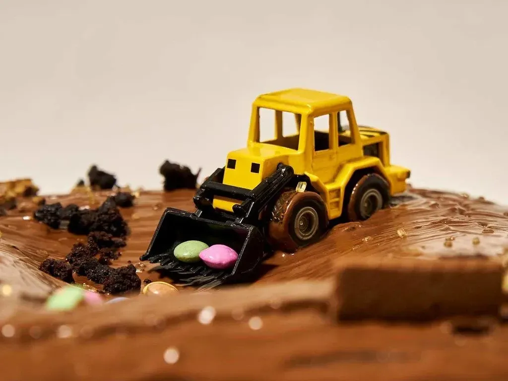 A close up image of a yellow tractor on top of a chocolate birthday cake.