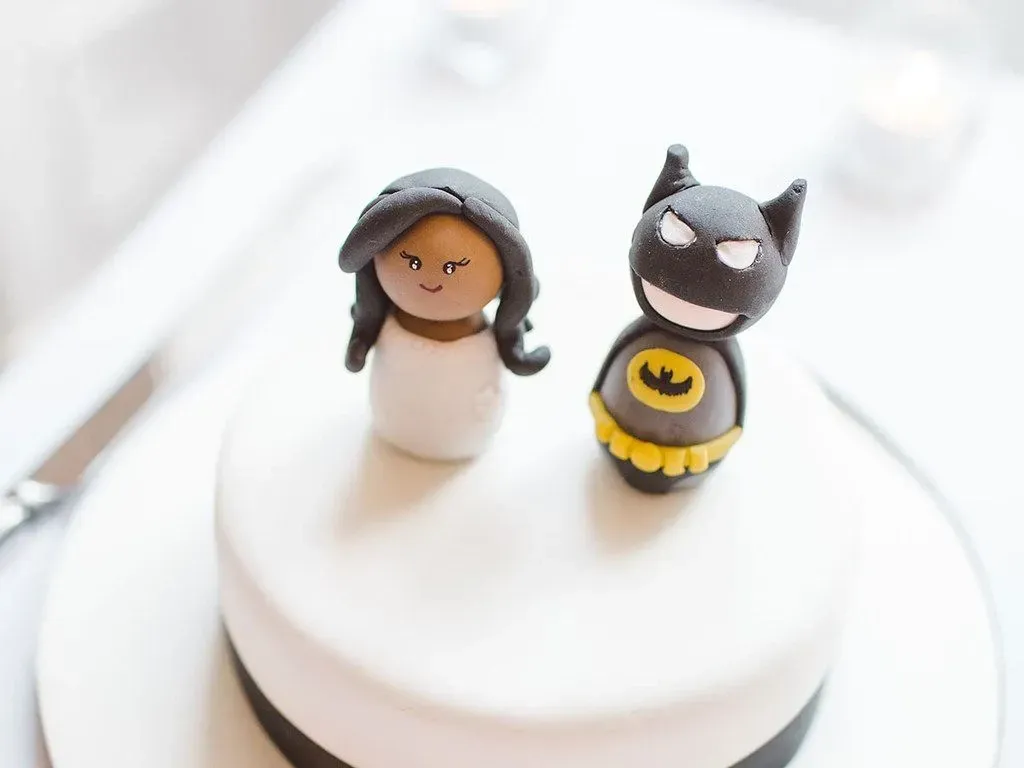 Two Batman cake toppers on top of a white cake.