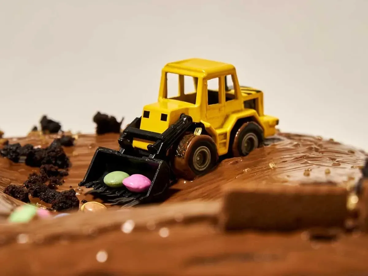 Chocolate cake with a yellow toy car digger on it shovelling sweeties.