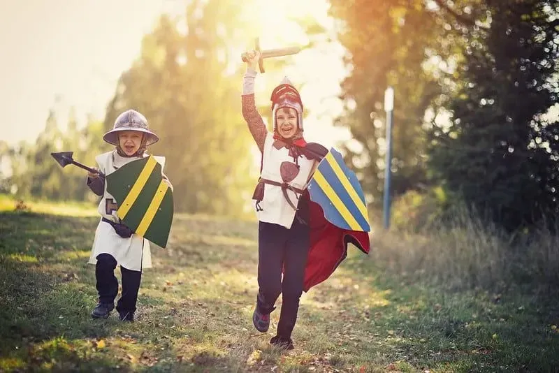 Kids dressed as knights running through the outdoors with shields.
