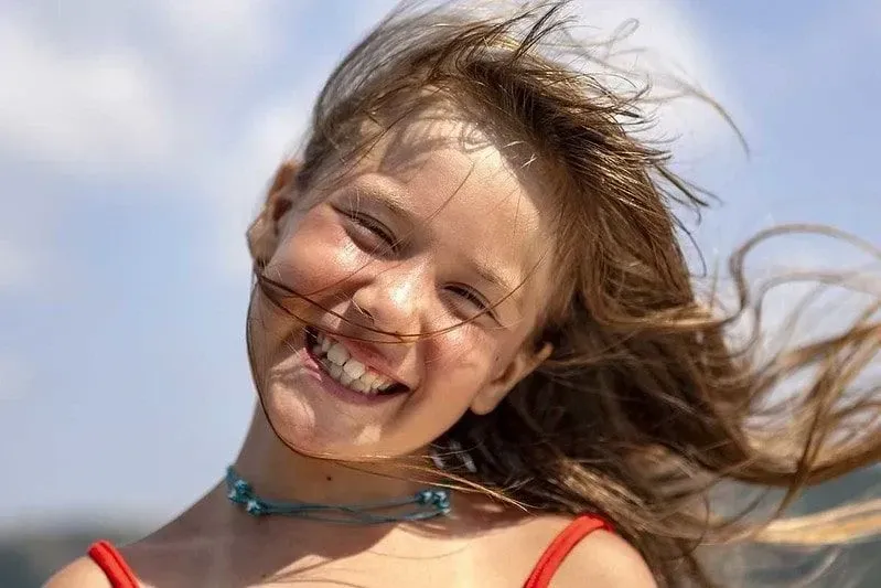 Young girl standing in the sun smiling as the wind blows her hair to one side.