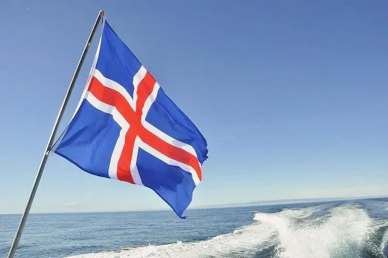 A blue, red and white Icelandic flag flying on the back of a boat.