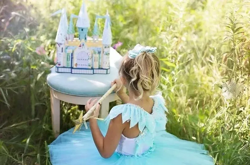 Little girl in blue fairy gown sitting in the grass with her mini blue castle.