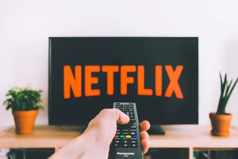 A remote pointing at a TV screen showing the Netflix logo at home. Image