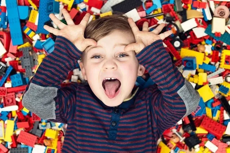 Boy in stripe long sleeve is lying down in the set of lego blocks.