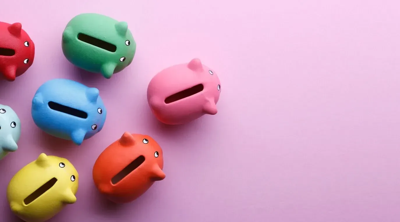 Multicoloured piggy banks spread out on a pink background.