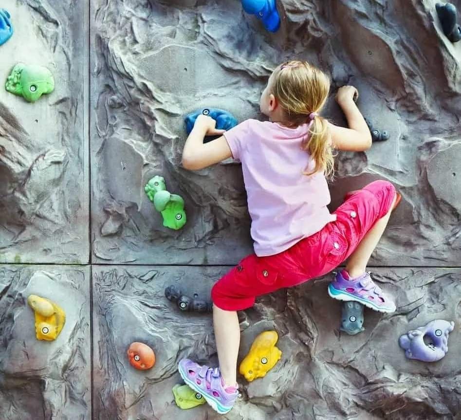 Little girl climbing on the wall with grips for hands and feet.