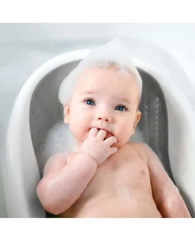 Baby in baby bath seat with soap on head. 