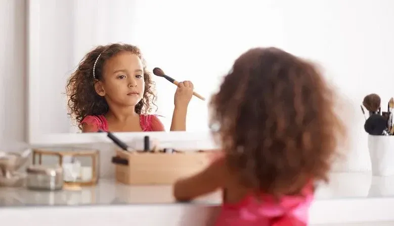 Girl having fun in her bedroom, doing makeup in the mirror on the dressing table. 