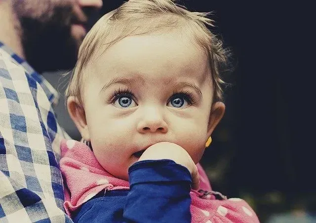 A baby girl with blue eyes sucking her thumb