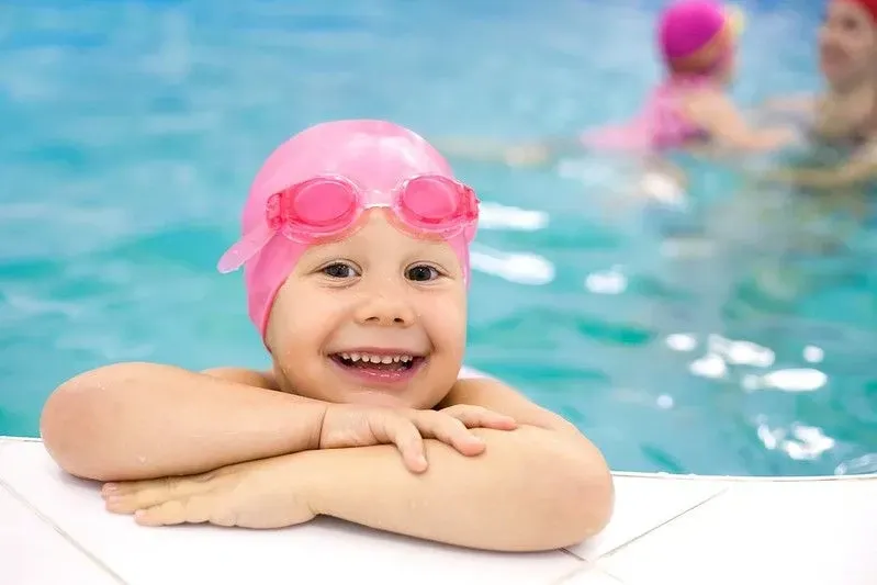 Young girl in pool, smiling, with pink cap