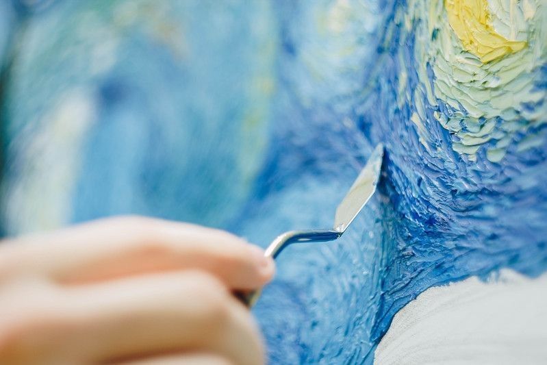 An Artist holding a mastekhin smeared in oil paint and painting Van Gogh's starry night replica.