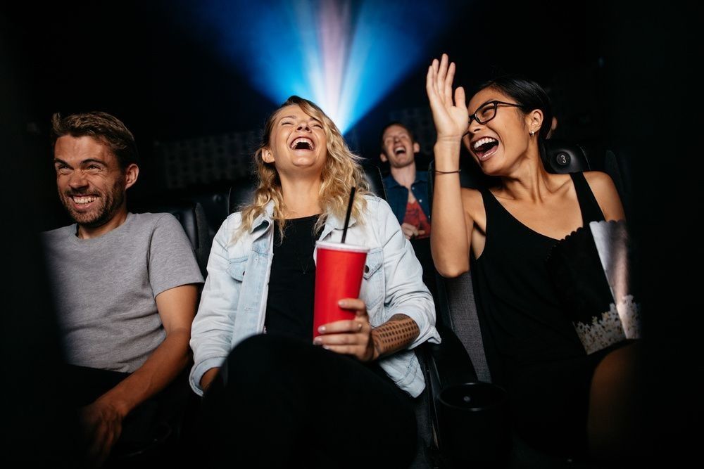 Group of people in theater with popcorn and drinks watching movie and laughing. 