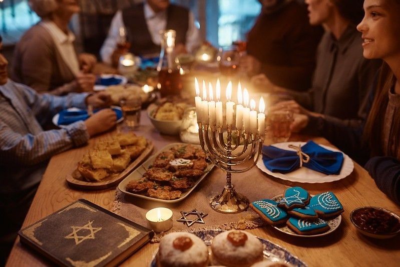 Lit candles in menorah with Jewish multigeneration family celebrating Hanukkah at dining table.