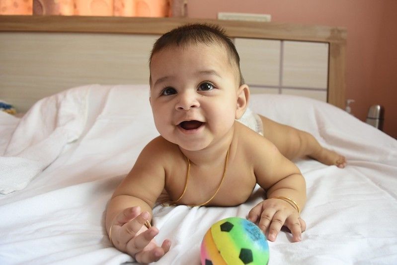 Indian newborn baby playing with ball on bed