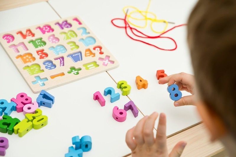 Kid learning numbers through game. Sensory activity with wooden numbers and shoe laces. Educations at home, pre-school education, Montessori methodology. sequence of numbers, arithmetic