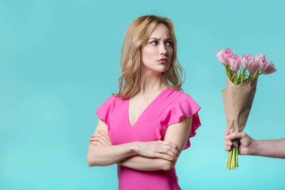  Offended girl is looking bouquet of tulips in male hand with hesitation