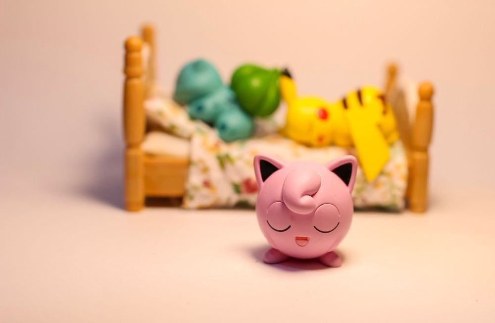 Jigglypuff figure in front of Pikachu and Bulbasaur figure sleeping on a bed