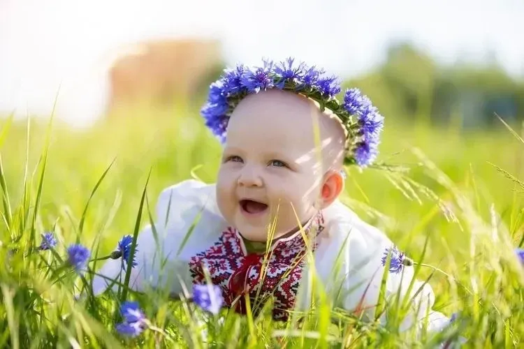 A happy little girl in national Belarusian clothes lies on the grass
