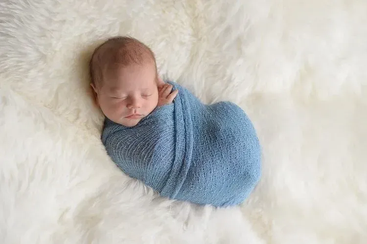 A newborn baby boy wrapped in a blue blanket is sleeping on white fur