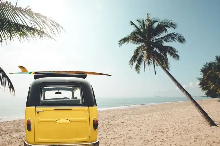 Rear of vintage car parked on the tropical beach with a surfboard on the roof