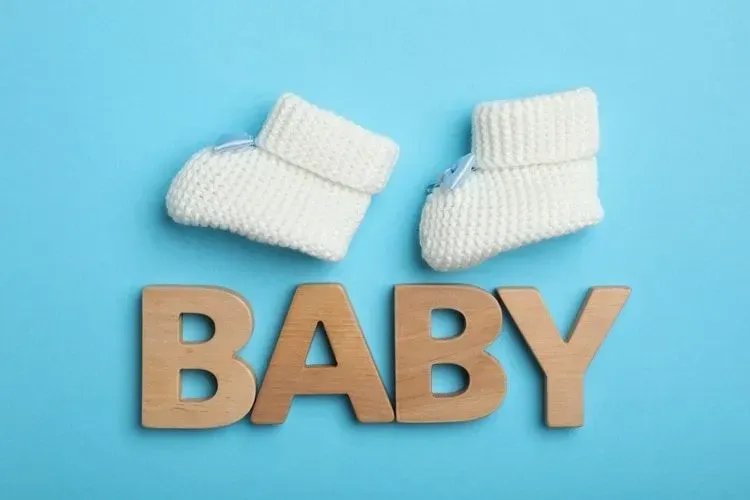 Wooden words BABY and white baby shoes on blue background