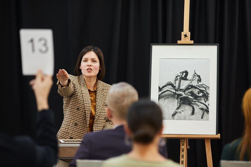 Auctioneer pointing at woman with sign and selling her the painting during auction.