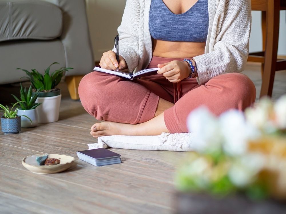 Woman journaling and manifesting in a diary as a routine at home. Writing down thoughts and feeling to reduce stress and improve mood. Calm ambiance with plants and crystals for inspiration