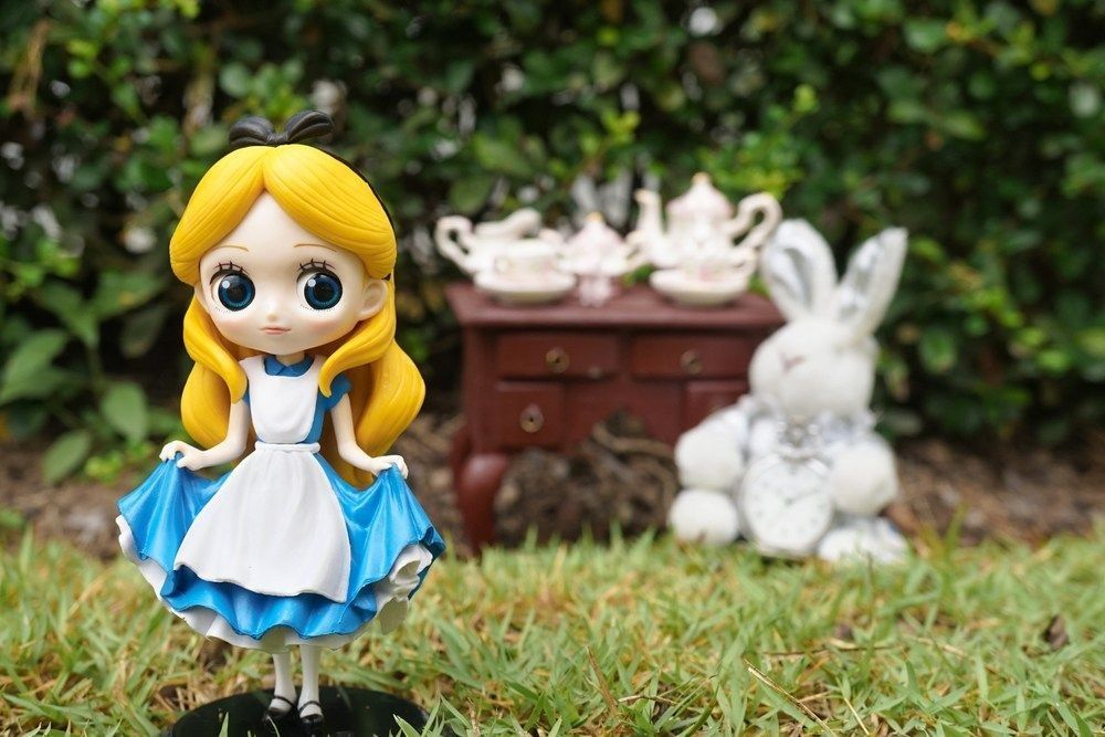 A photo of Alice's adventure in Wonderland stands in front of the mad tea party with a white rabbit nearby.