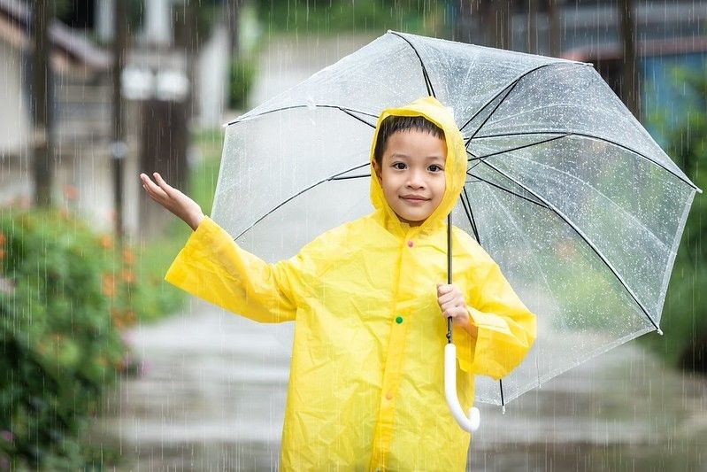 Happy little boy having fun playing in the April rain.