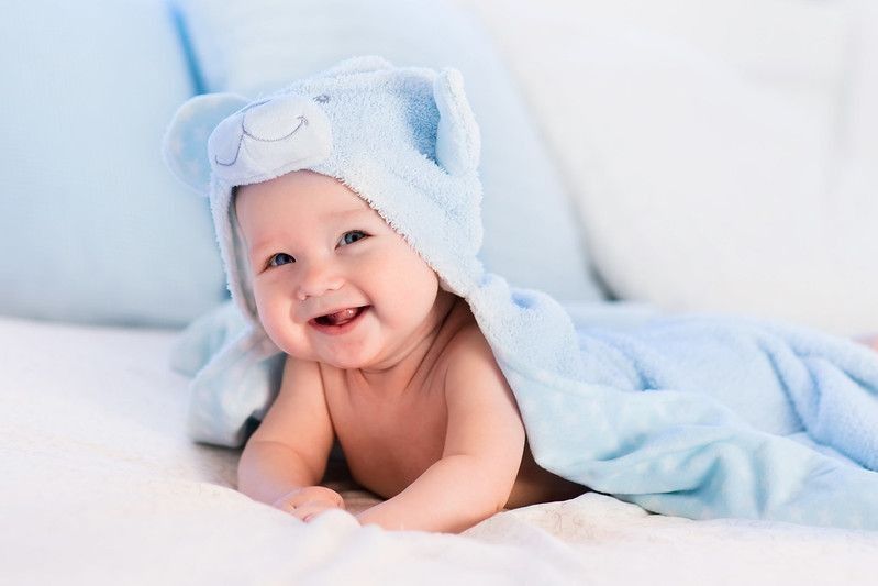 Baby boy wearing diaper and blue towel in white sunny bedroom.