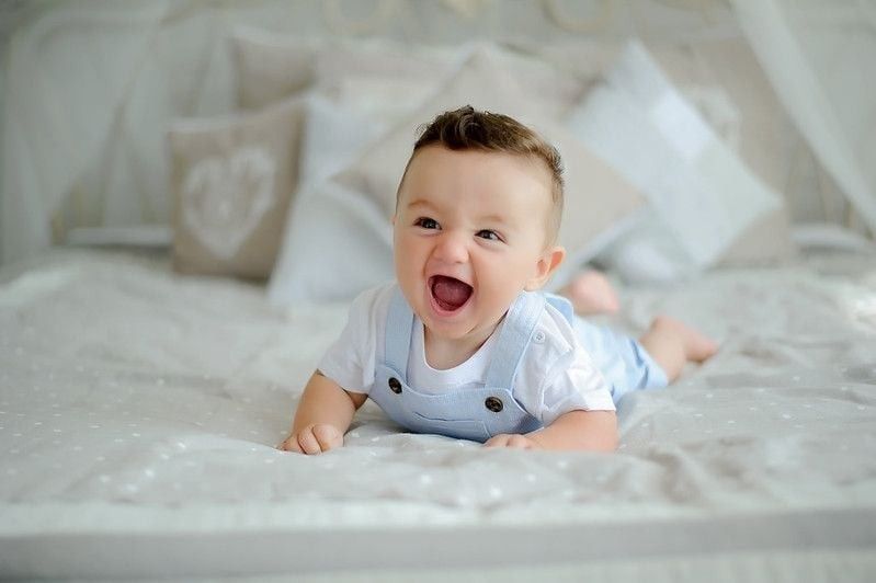 Cute boy sitting on the white blanket at the bed.