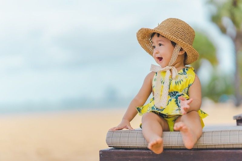 Baby girl wearing summer dress and hat on beach
