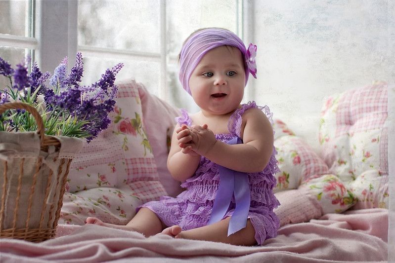 Baby girl in lavender dress with flower headband at interior with lavender.