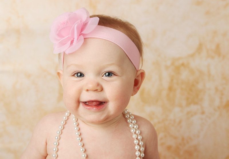Adorable young baby girl wearing a vintage pearl necklace and pink rose headband.