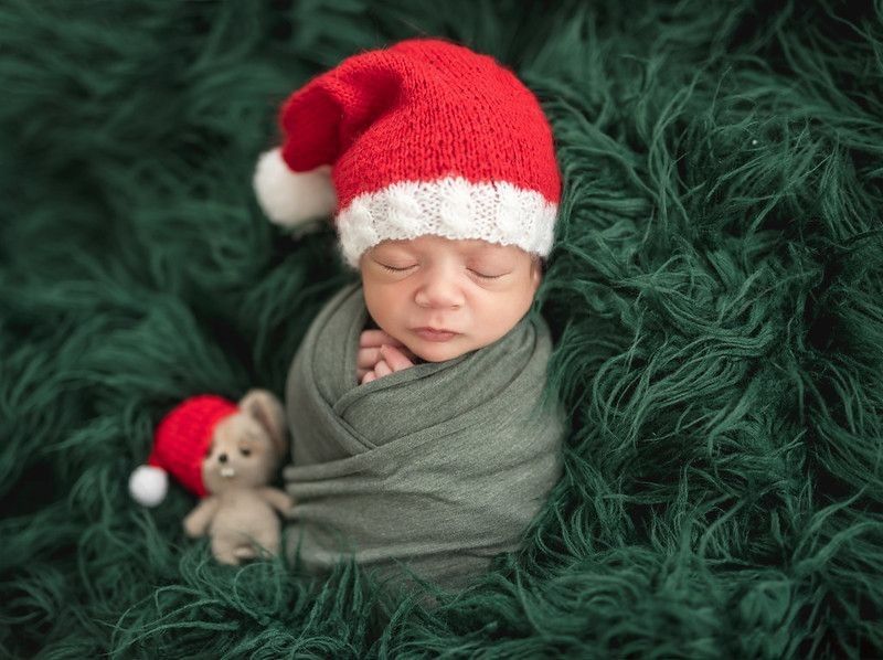 Newborn baby wearing Christmas hat sleeping on green fur blanket