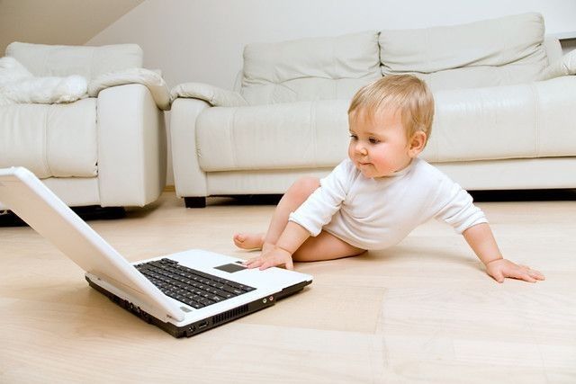 The laptop appears to be of particular interest to the child, who leans forward to get a closer look at the screen.