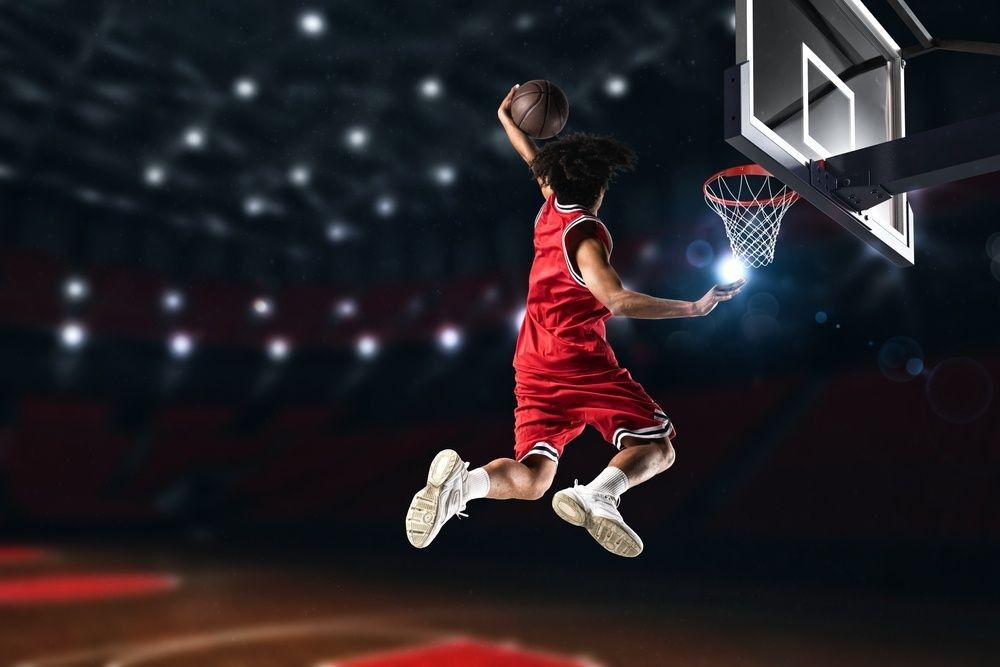 Basketball player in red uniform jumping high to make a slam dunk to the basket.