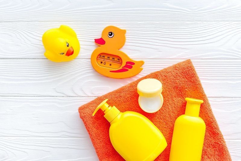Yellow rubber duck,towel, cream, shampoo on white wooden background.
