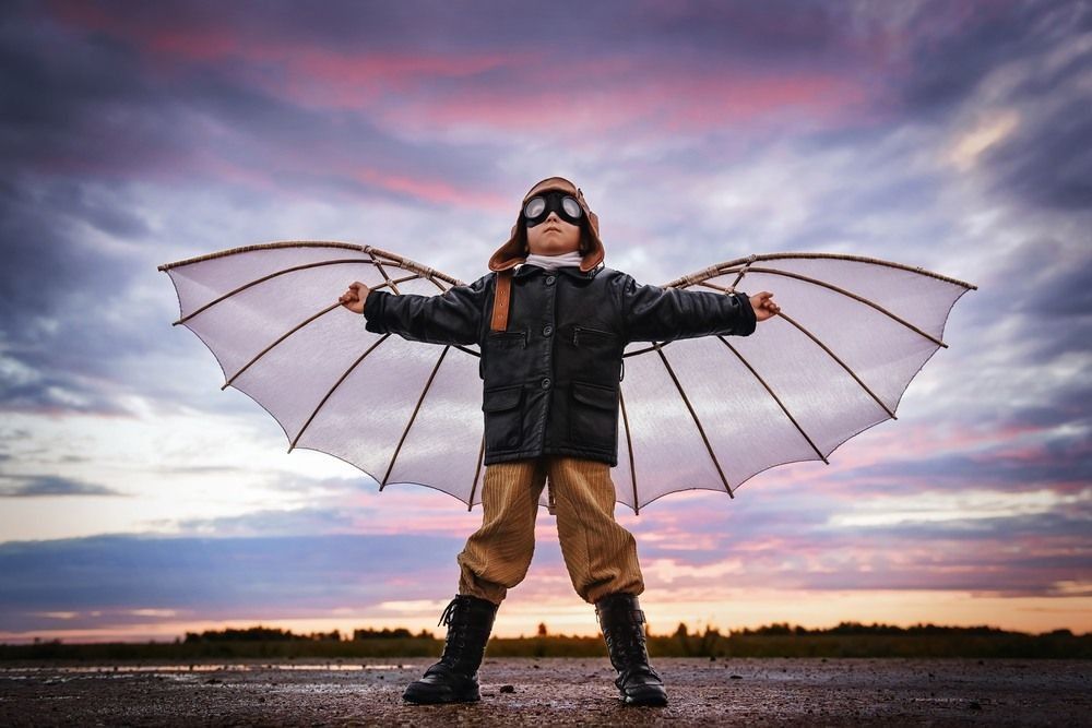 Boy with wings at sunset imagines himself a pilot and dreams of flying.