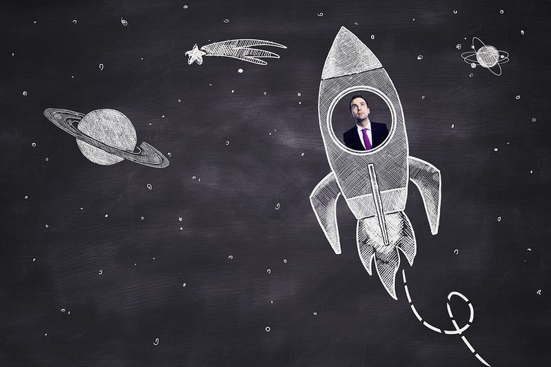 Startup concept with businessman inside abstract space ship sketch on chalkboard background.
