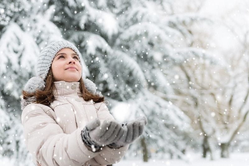 Teenage girl looking in the sky and catching a snowflakes.