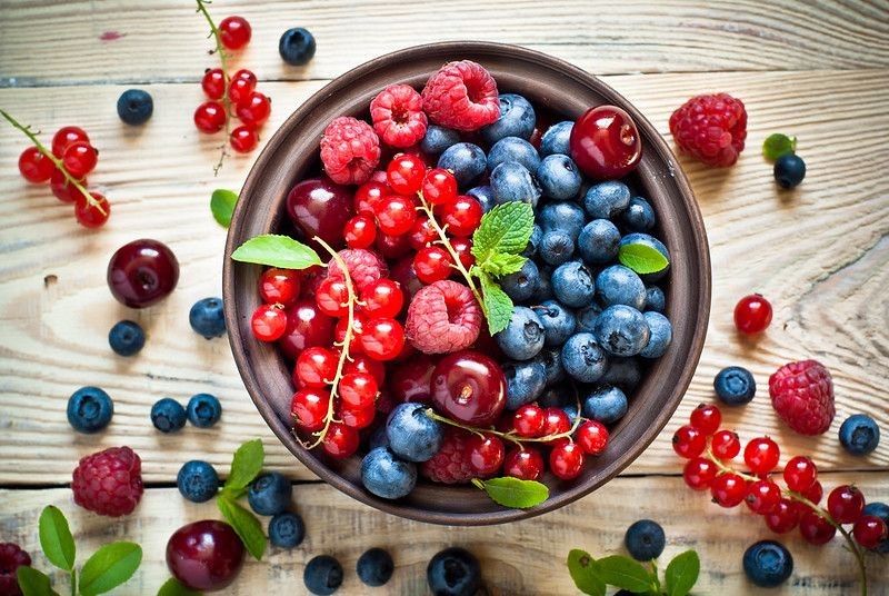 Various summer fruits in a bowl on rustic wooden table.