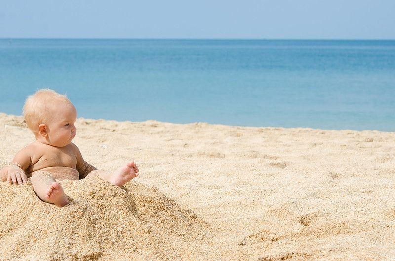 Newborn baby sitting on sand on a beach.