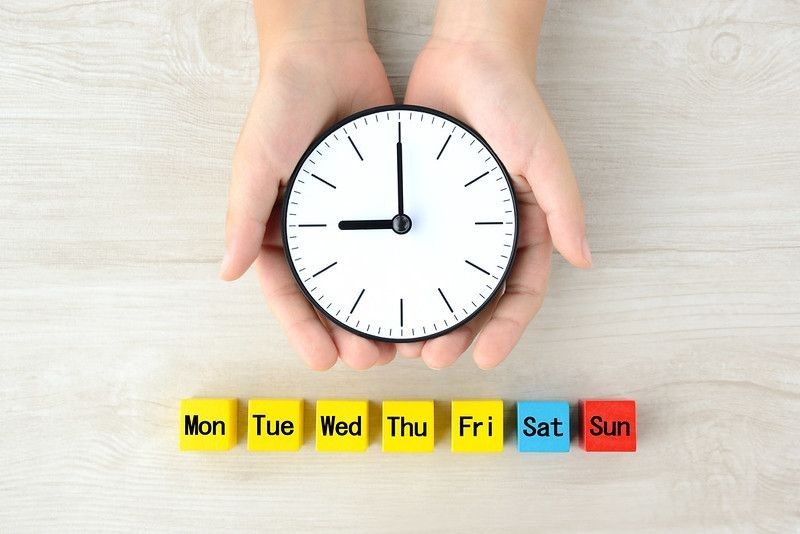 Clock covered by child's hands and colorful wooden blocks with omitted day of week words