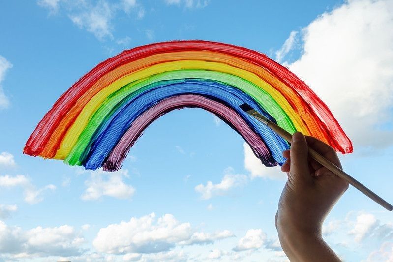 Kid hand painting colorful rainbow on window.