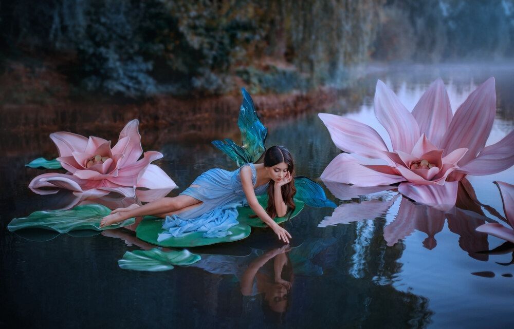 A little cute fairy with butterfly wings lies on green water lily leaf.